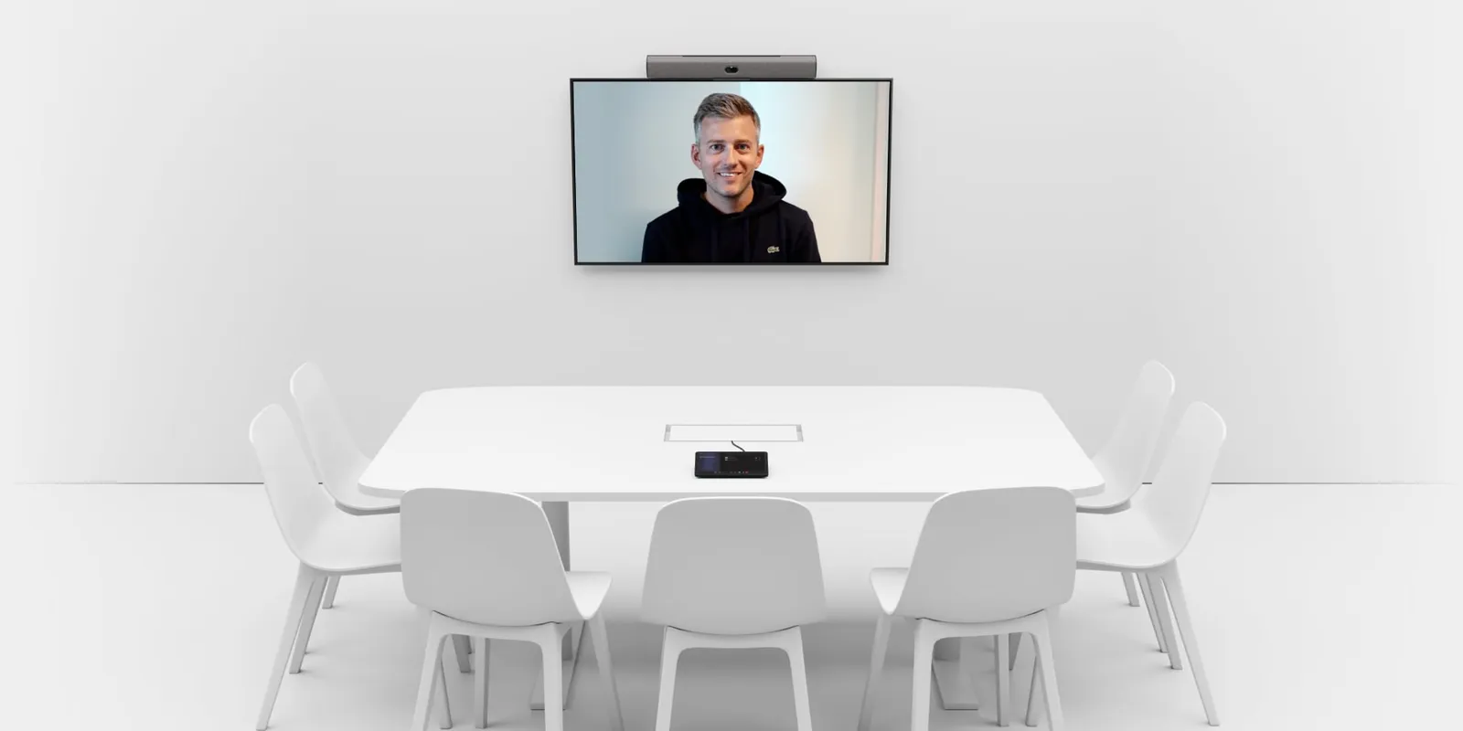 A meeting room with a Neat Bar mounted above a wall display showing a remote participant, and a Neat Pad controller on the table
